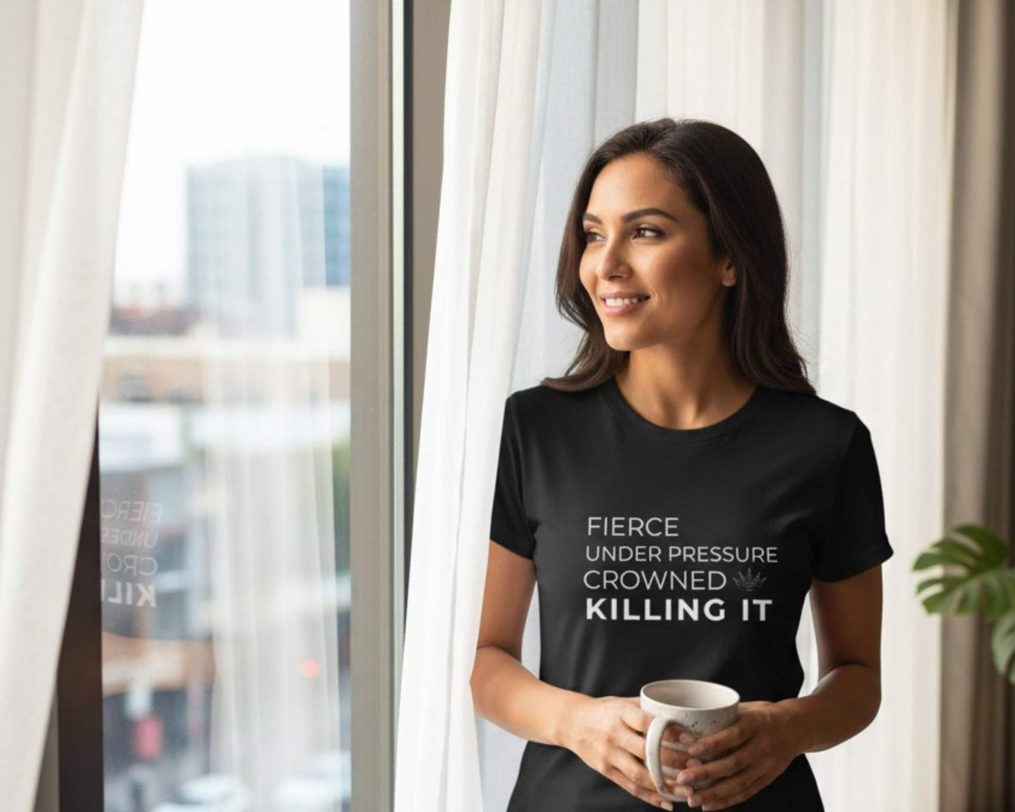 Woman wearing a black t-shirt with motivational text, holding a mug indoors.