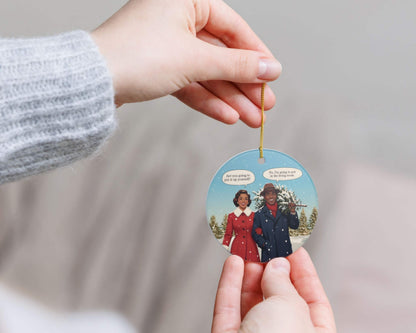 Hand holding a Christmas ornament with a couple on it against a neutral background
