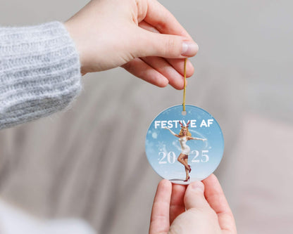 Person holding a Christmas ornament with 'Festive AF 2025' text and design.