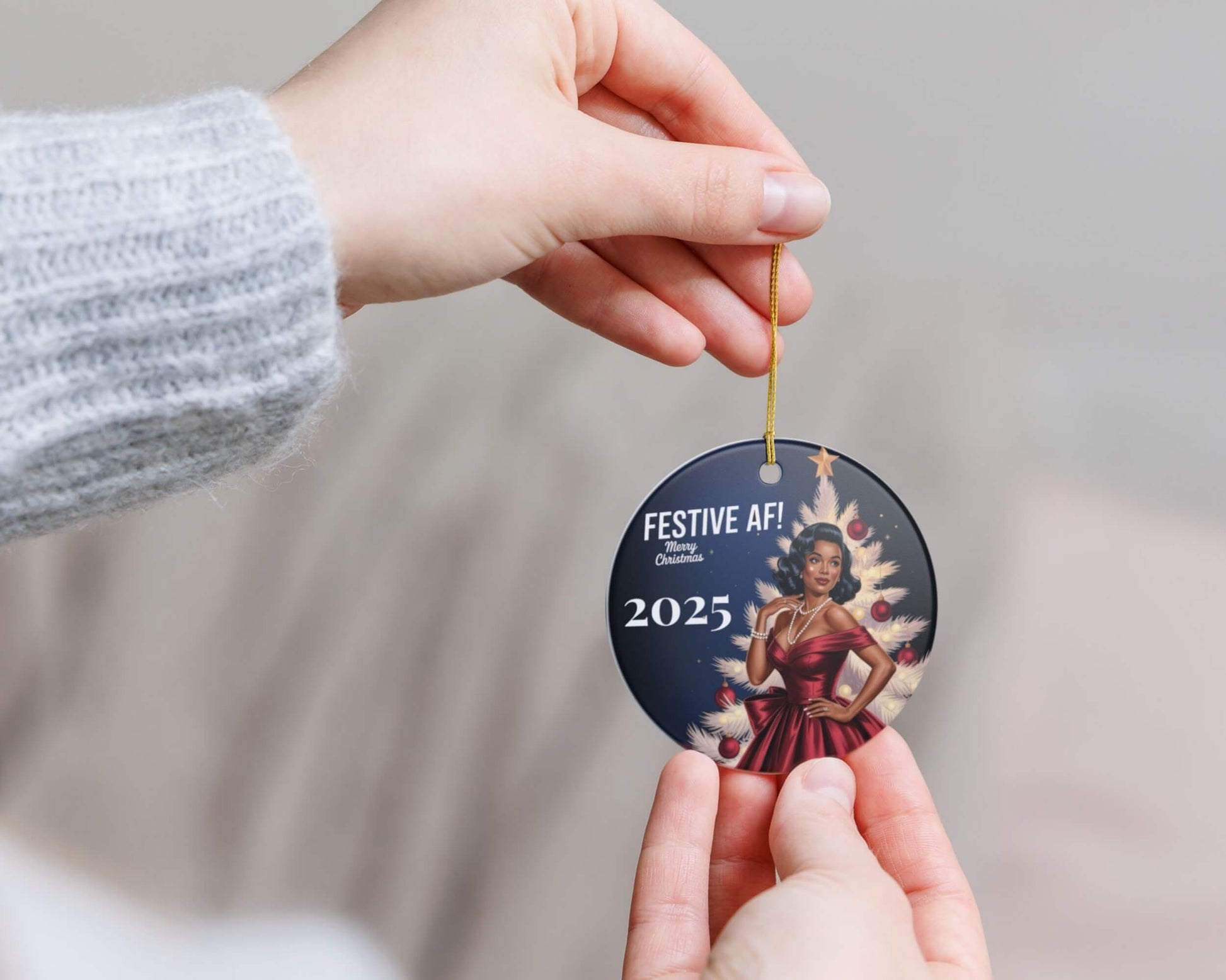 Hand holding a Christmas ornament with 'Festive AF! 2025' text and a person in a red dress.